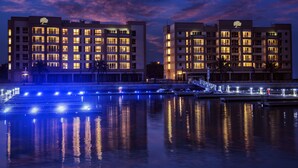 Un hotel de varios pisos con balcones, vista al agua y el reflejo de luces sobre el agua.