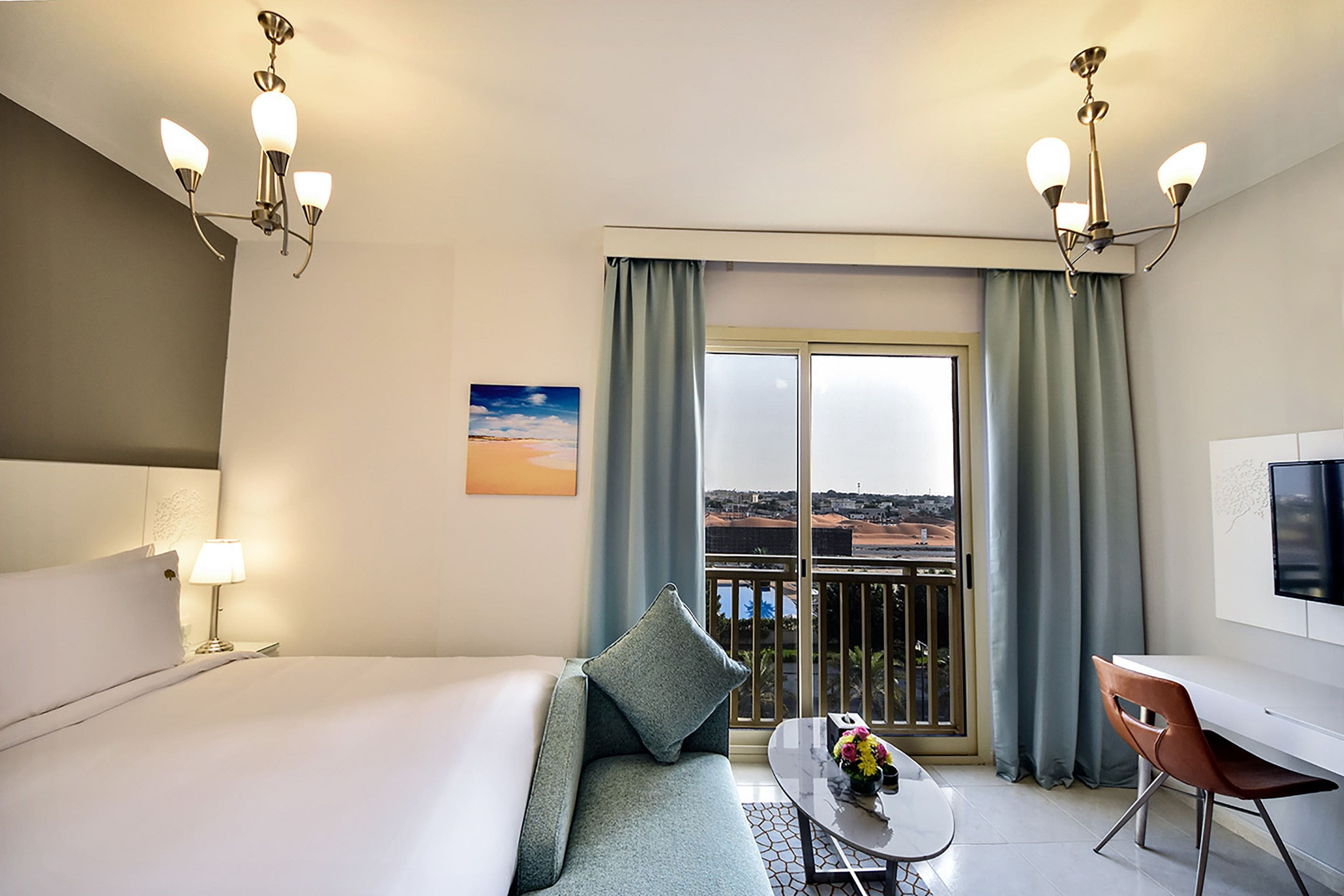 A hotel room with a bed, a sofa, a dining table with chairs, a TV, and a balcony with a view.