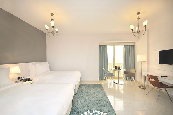 A hotel room with two beds, a desk, a chair, a TV, and a window with curtains. - Jannah Hotel Apartments & Villas (Ras Al Khaimah)