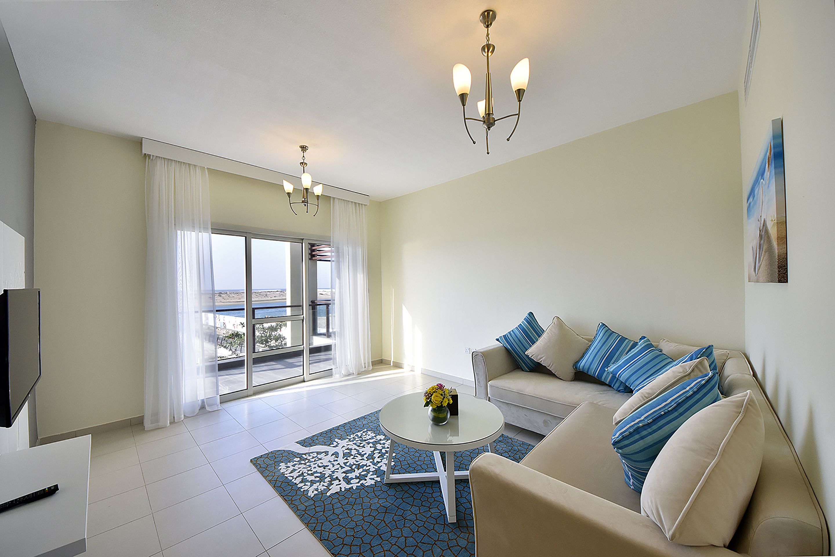A modern living room with a sofa, a coffee table, a TV, and a balcony with curtains.