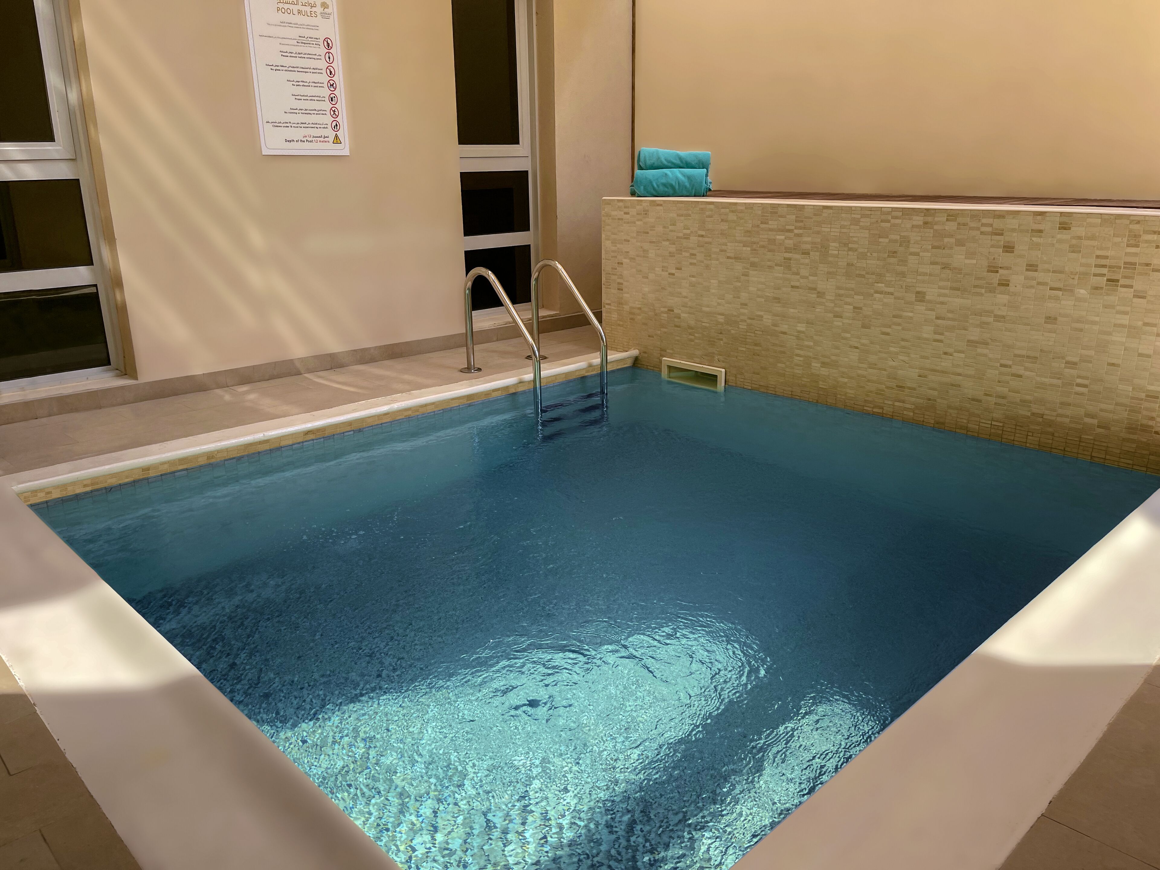 Ein Hallenbad mit klarem Wasser, einer Metallleiter und einer gefliesten Wand.