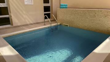Ein Hallenbad mit klarem Wasser, einer Metallleiter und einer gefliesten Wand.