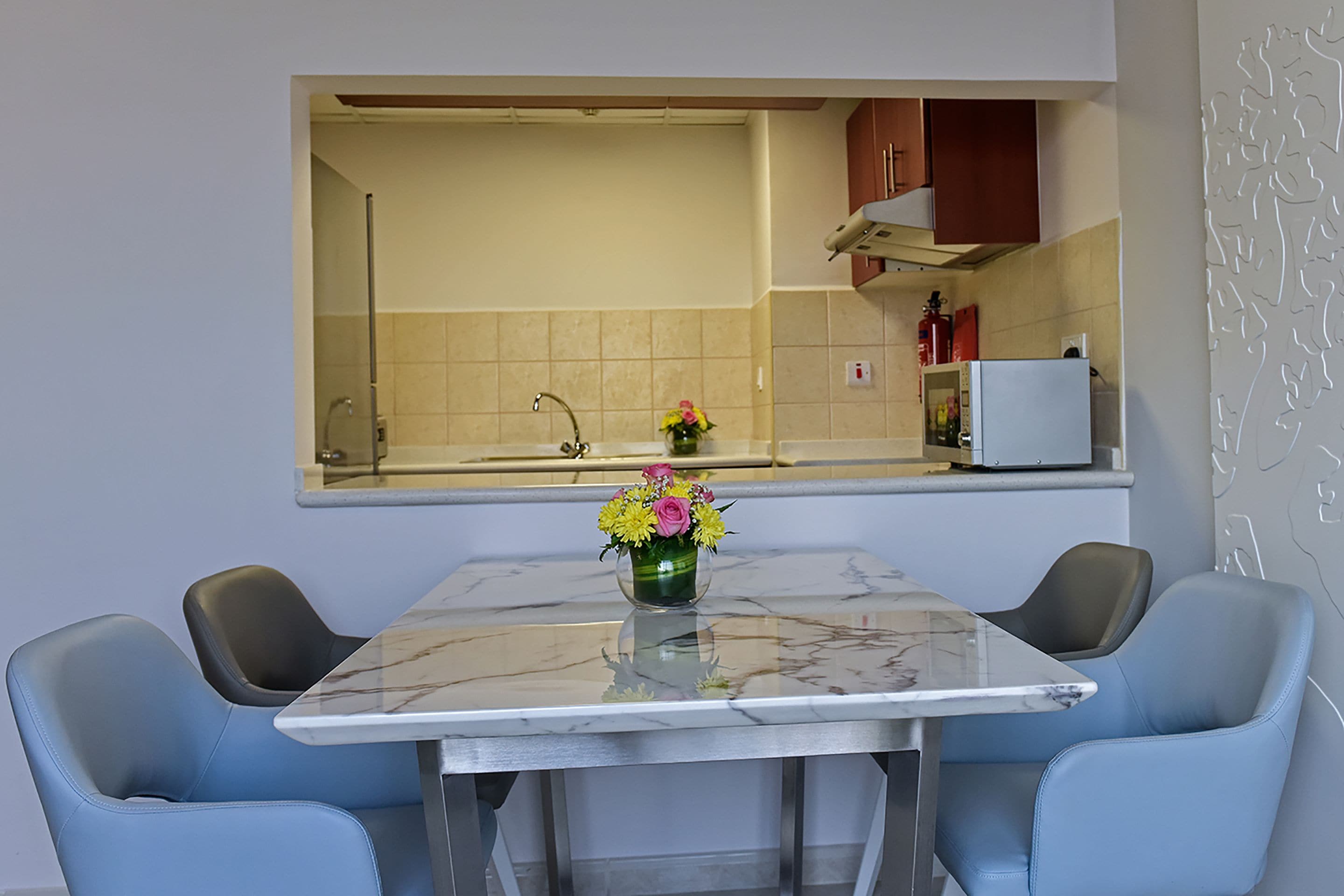 A modern kitchen with a marble countertop, two blue chairs, and a vase of flowers.