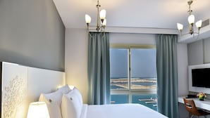 Habitación de hotel con cama, escritorio, televisor y vista al mar.