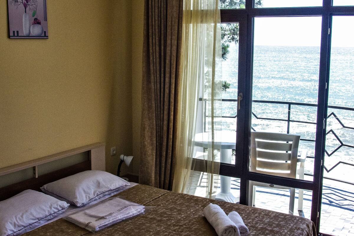 A hotel room with a bed, a window with a view of the sea, and a chair outside the window.