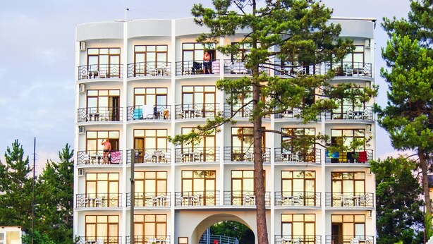 Un hotel de varios pisos con balcones, un arco central y vista al agua.