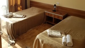 Habitación de hotel con dos camas, un escritorio con lámpara, un cuadro en la pared y una ventana con cortinas.