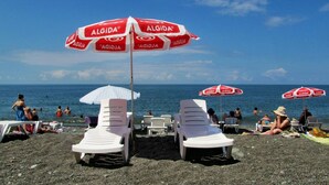 Una playa con sillas reclinables blancas y sombrillas rojas, con la marca 'ALGIDA'.