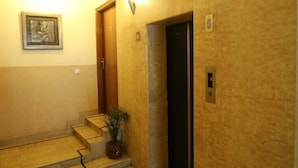 A hallway with a wooden door, a wall-mounted light, and a framed picture. - Hotel Singh Sahib (New Delhi)