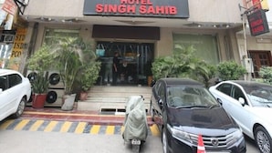 A hotel named "Hotel Singh Sahib" with a signboard, multiple windows, and a few parked cars in front. - Hotel Singh Sahib (New Delhi)