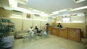 A reception area with a reception desk, two sofas, a coffee table, and a large plant. - Hotel Singh Sahib (New Delhi)