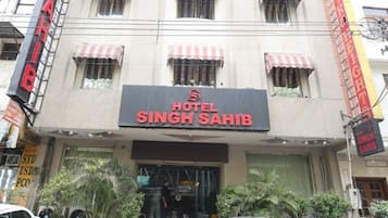 Un hôtel appelé « Hotel Singh Sahib », avec une enseigne, de nombreuses fenêtres et quelques voitures garées devant.