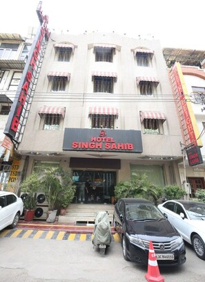 Hotel "Hotel Singh Sahib" met een bord, meerdere ramen en enkele geparkeerde auto's voor de gevel.