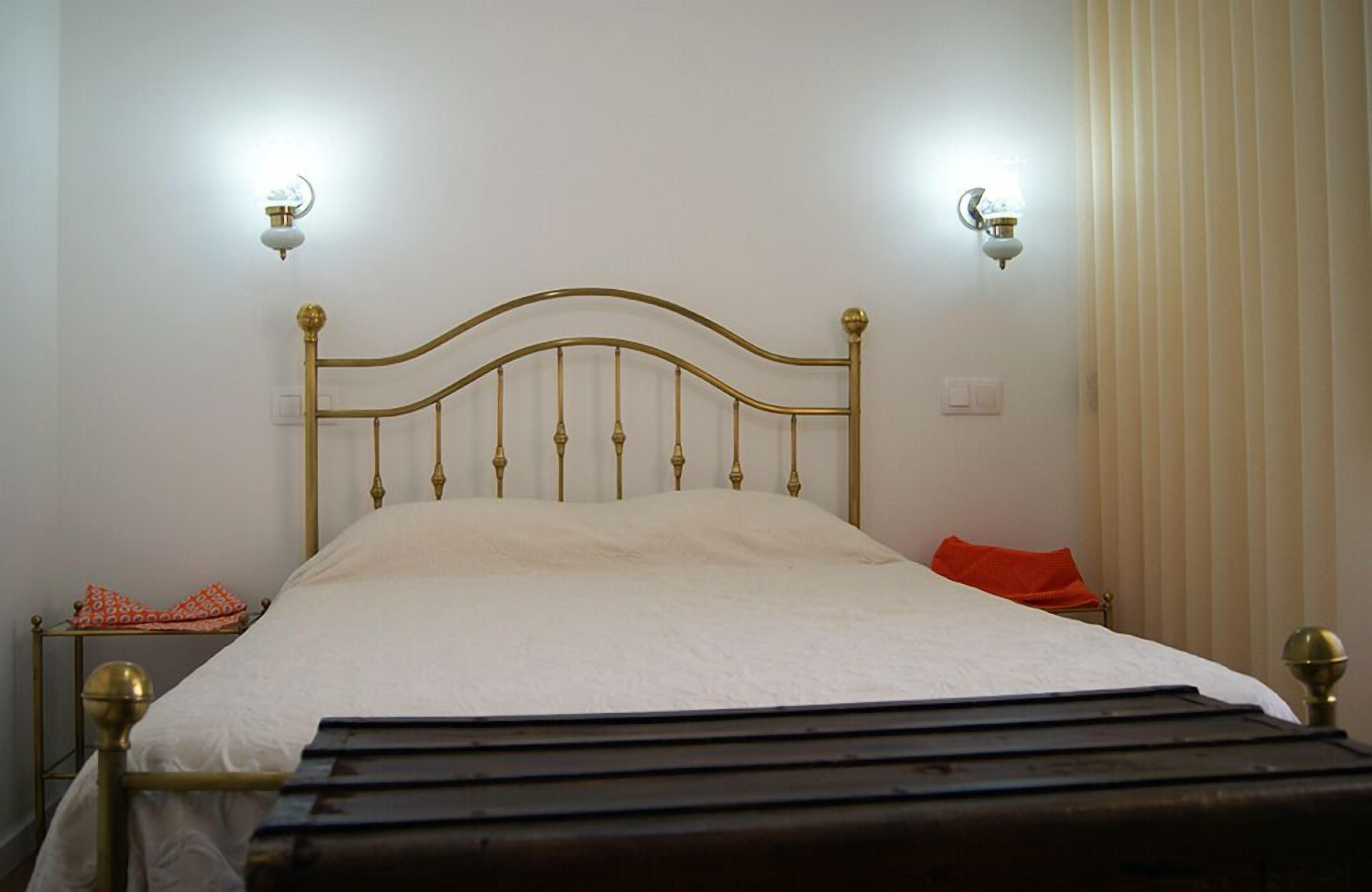 A bed with a headboard, two wall-mounted light fixtures, a bedside table, and a curtain.