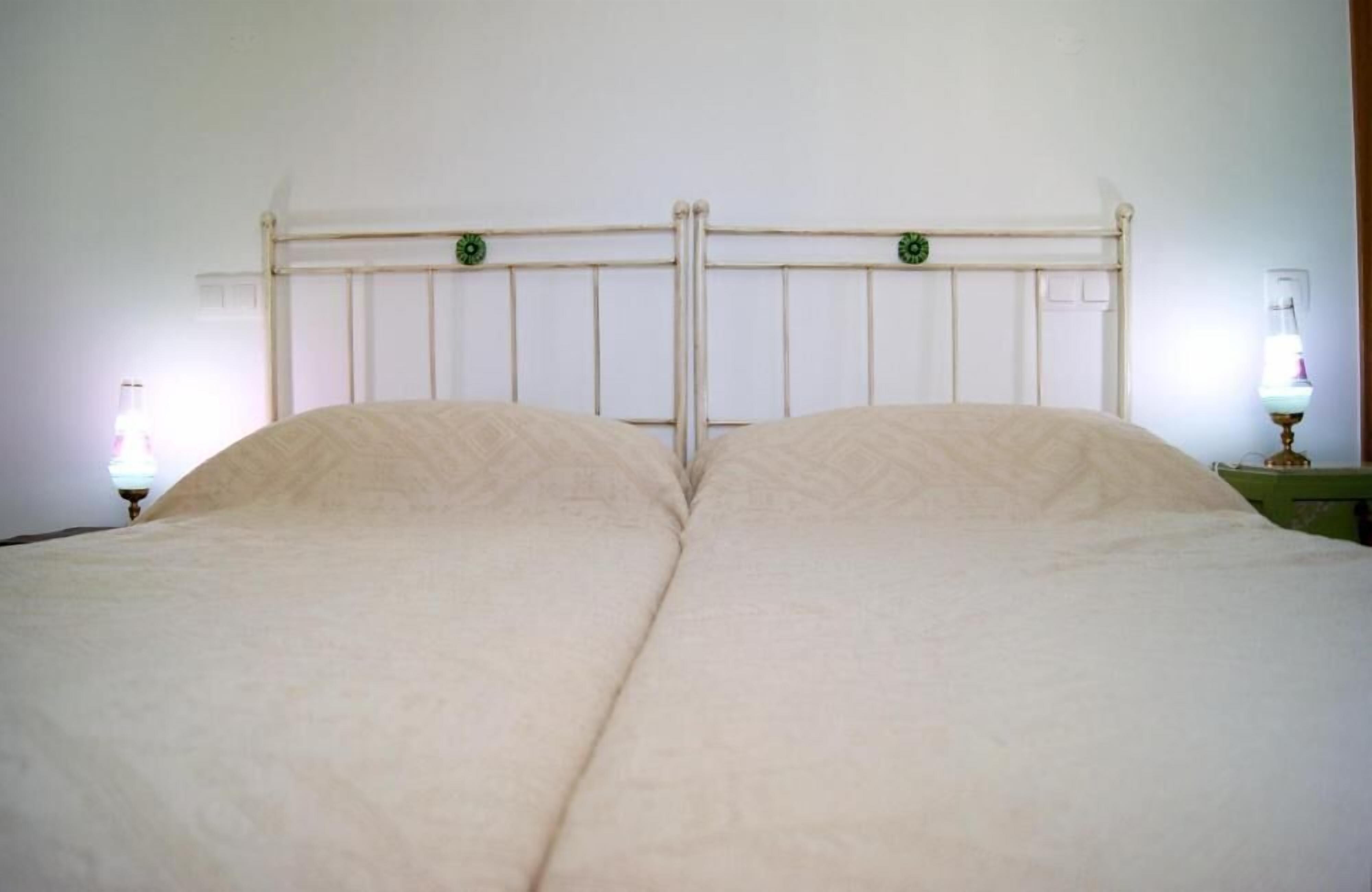 Una cama con cabecera de madera, dos lámparas de noche y un adorno verde en la cabecera.