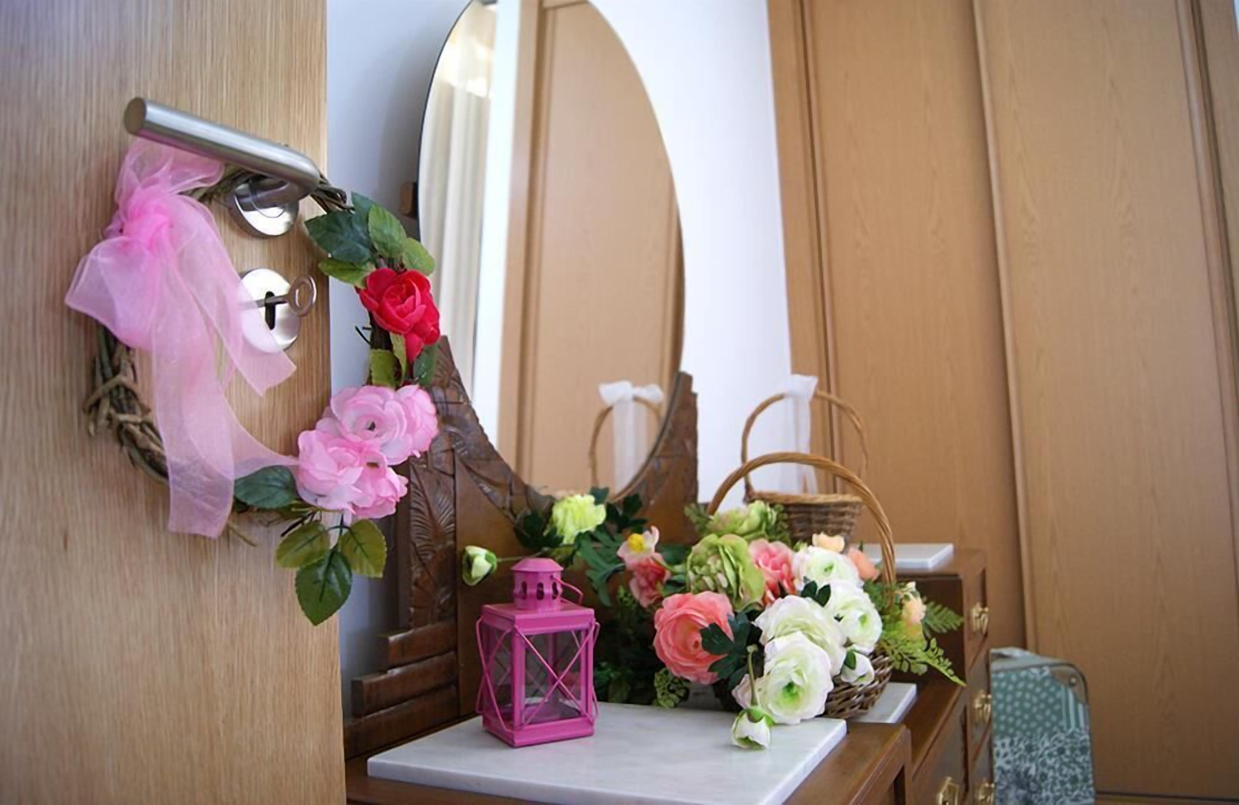 Een houten dressoir met spiegel, een roze lantaarn en een bloemstuk.