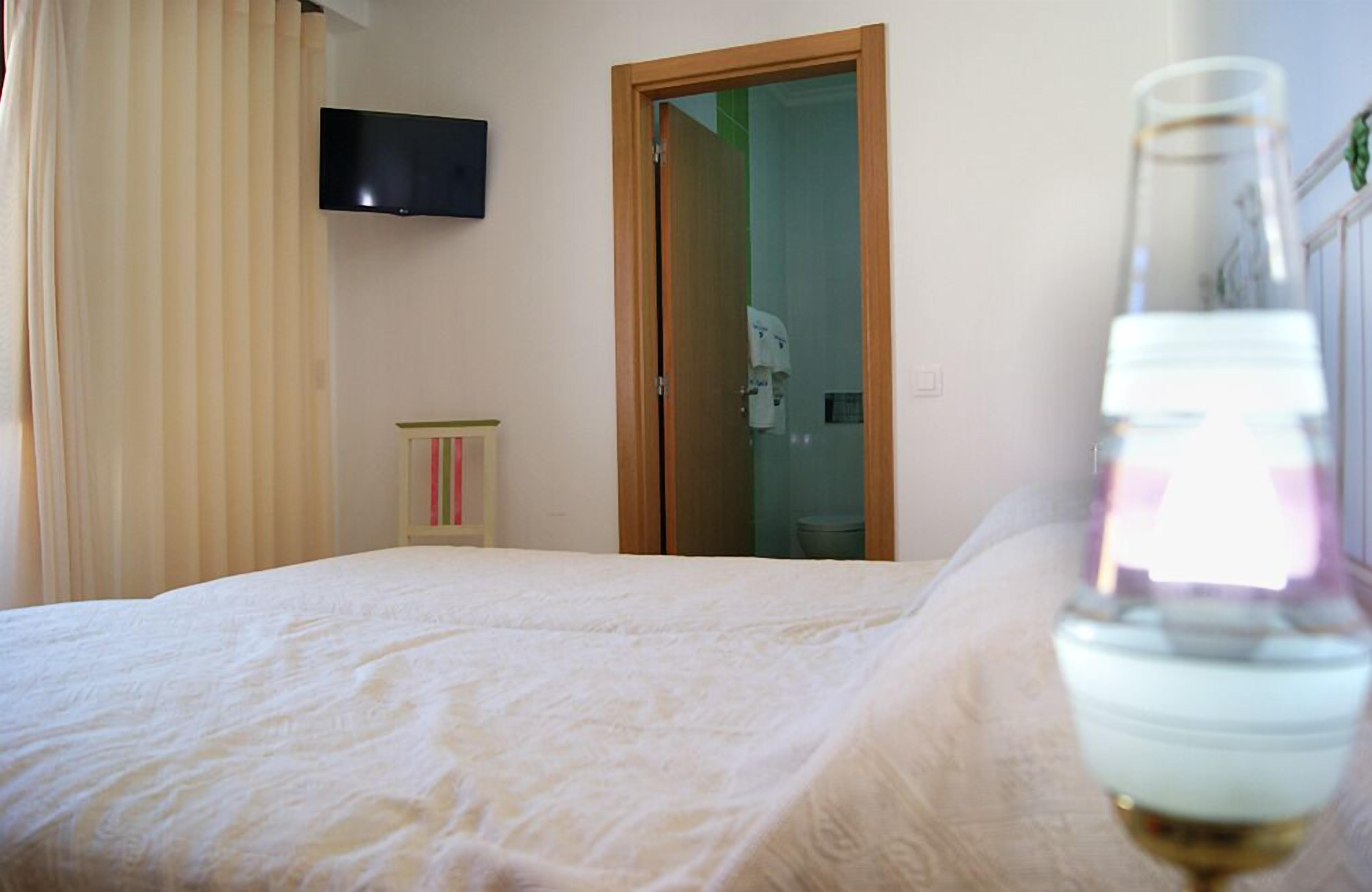 Un dormitorio con una cama, un televisor montado en la pared y una puerta que da al baño.