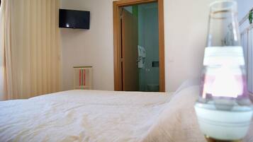 Un dormitorio con una cama, un televisor montado en la pared y una puerta que da al baño.