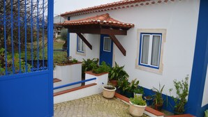 Une maison avec une porte et des fenêtres bleues, un toit recouvert de tuiles et des plantes en pot disposées autour de l’entrée.
