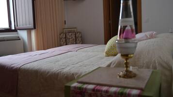 Ein Schlafzimmer mit einem Bett, einem Nachttisch mit Lampe, einem Fenster mit Vorhängen und einem an der Wand befestigten Fernseher.