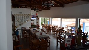 Un grand espace dédié à la salle à manger, avec plusieurs tables et chaises, un mur décoré d’assiettes et un écran de télévision.