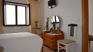 Une chambre à coucher comprenant un lit, une commode, une chaise et un téléviseur fixé au mur.