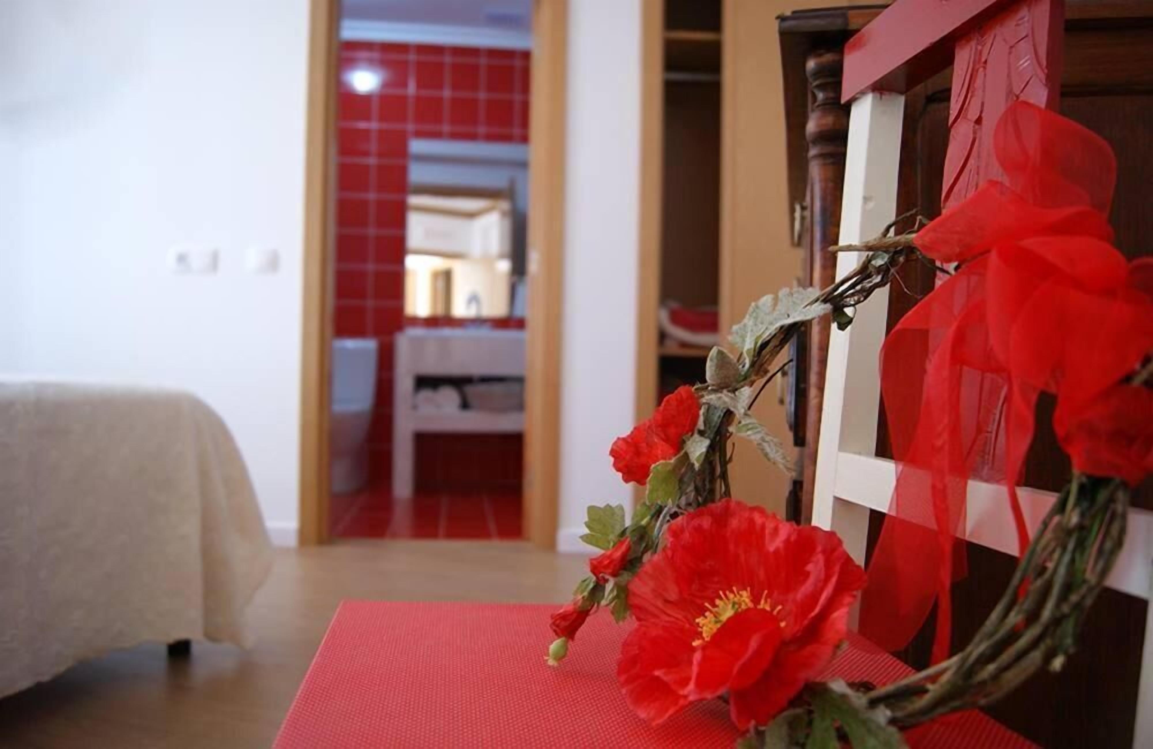 A room with a bed, a red mat, and a vase with red flowers.