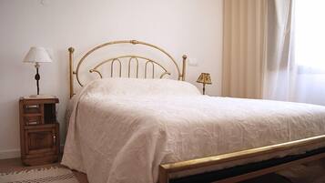 A neatly made bed with a gold frame, a bedside table with a lamp, and a window with curtains.