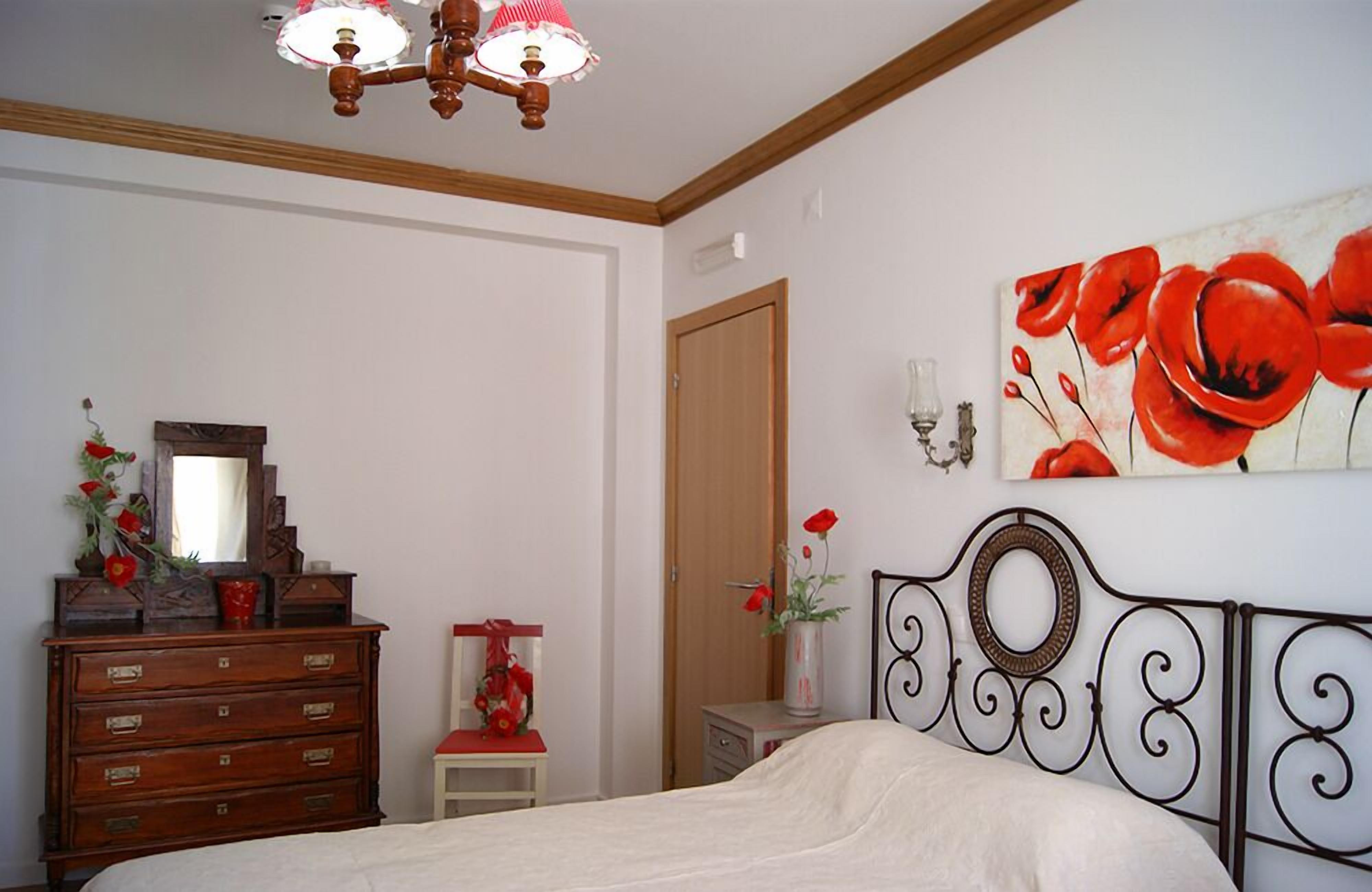 A bedroom with a bed, dresser, and a painting of red flowers on the wall.