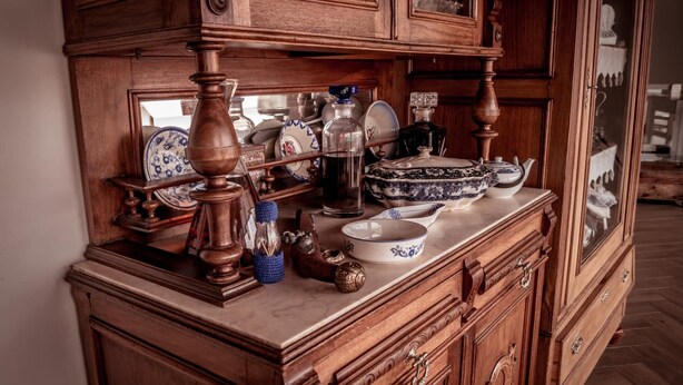 Un meuble en bois doté de portes en verre, contenant divers ustensiles de cuisine, comme une théière, un bol et une bouteille.