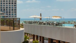 A rooftop pool area with lounge chairs and umbrellas, overlooking a body of water and a tall building. - Dream Beach TLV Boutique Hotel (Tel Aviv)