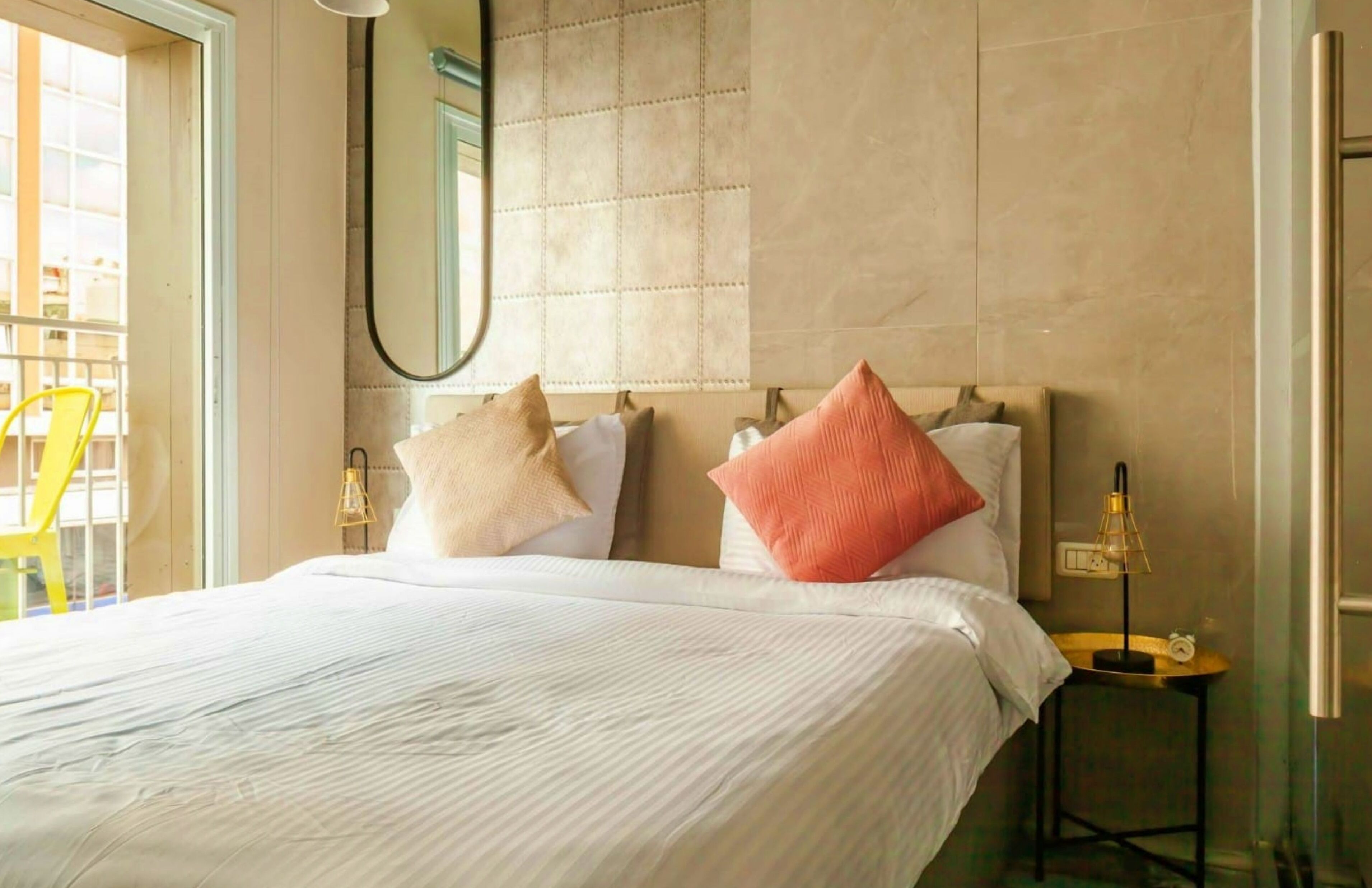 Een hotelkamer met een groot bed, een nachtkastje met een lamp en een spiegel aan de muur.