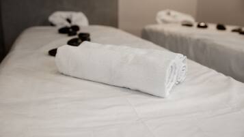 Una cama bien tendida con una toalla blanca enrollada y una pequeña pila de piedras negras encima.