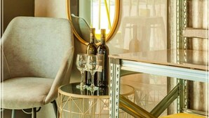 A hotel room with a large mirror, a sofa, a small round table with bottles and glasses, and a TV mounted on a metal structure. - Dream Beach TLV Boutique Hotel (Tel Aviv)