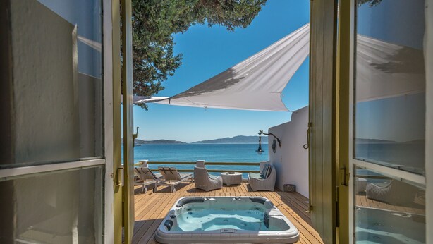 Puerta abierta que da a una terraza con jacuzzi, sillones de descanso y vista al mar.