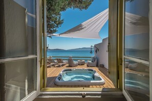 An open door leading to a deck with a hot tub, lounge chairs, and a view of the sea. - Villa Lord (Milos)