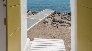 Vista a través de una puerta que da a una playa con cielo despejado y mar tranquilo.