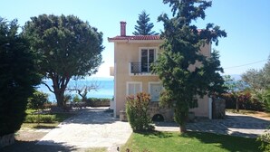 Una casa de dos pisos con un camino de piedra que conduce a la entrada, rodeada de árboles y con vista al mar.
