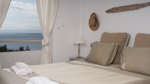 Un dormitorio con cama, toallas, una lámpara, un sombrero en la pared y vista al mar.