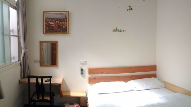 Une chambre à coucher avec un lit, un bureau, une chaise, un miroir et une fenêtre avec des rideaux.