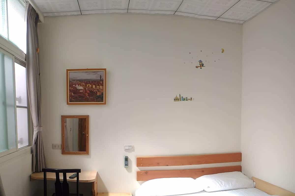 Un dormitorio con cama, escritorio, silla, espejo y ventana con cortinas.