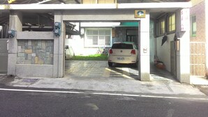 Une voiture était garée sous une structure de stationnement couverte, adossée à un mur en pierre, et un panneau indiquait la présence de toilettes publiques.