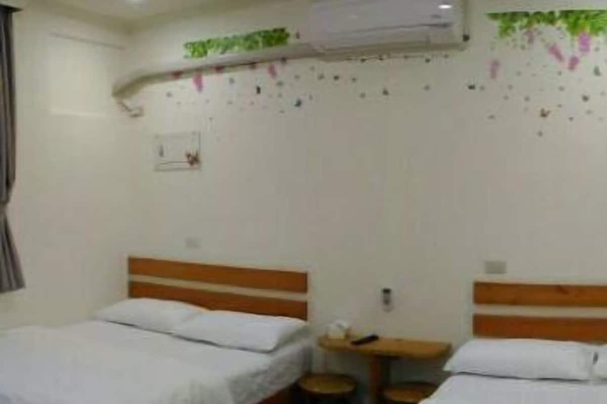 Una habitación con dos camas individuales, una mesita pequeña y un equipo de aire acondicionado instalado en la pared.
