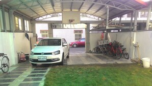 Un espace de stationnement couvert où se trouvent une voiture blanche, des vélos et une voiture rouge garée à l’extérieur.