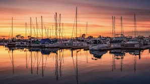 Eine Marina mit mehreren Booten, die an ruhigem Wasser festgemacht sind, wobei der Abendhimmel sich im Wasser spiegelt.