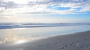 Ein Strand mit Fußspuren im Sand und Wellen, die sich dem Ufer nähern.