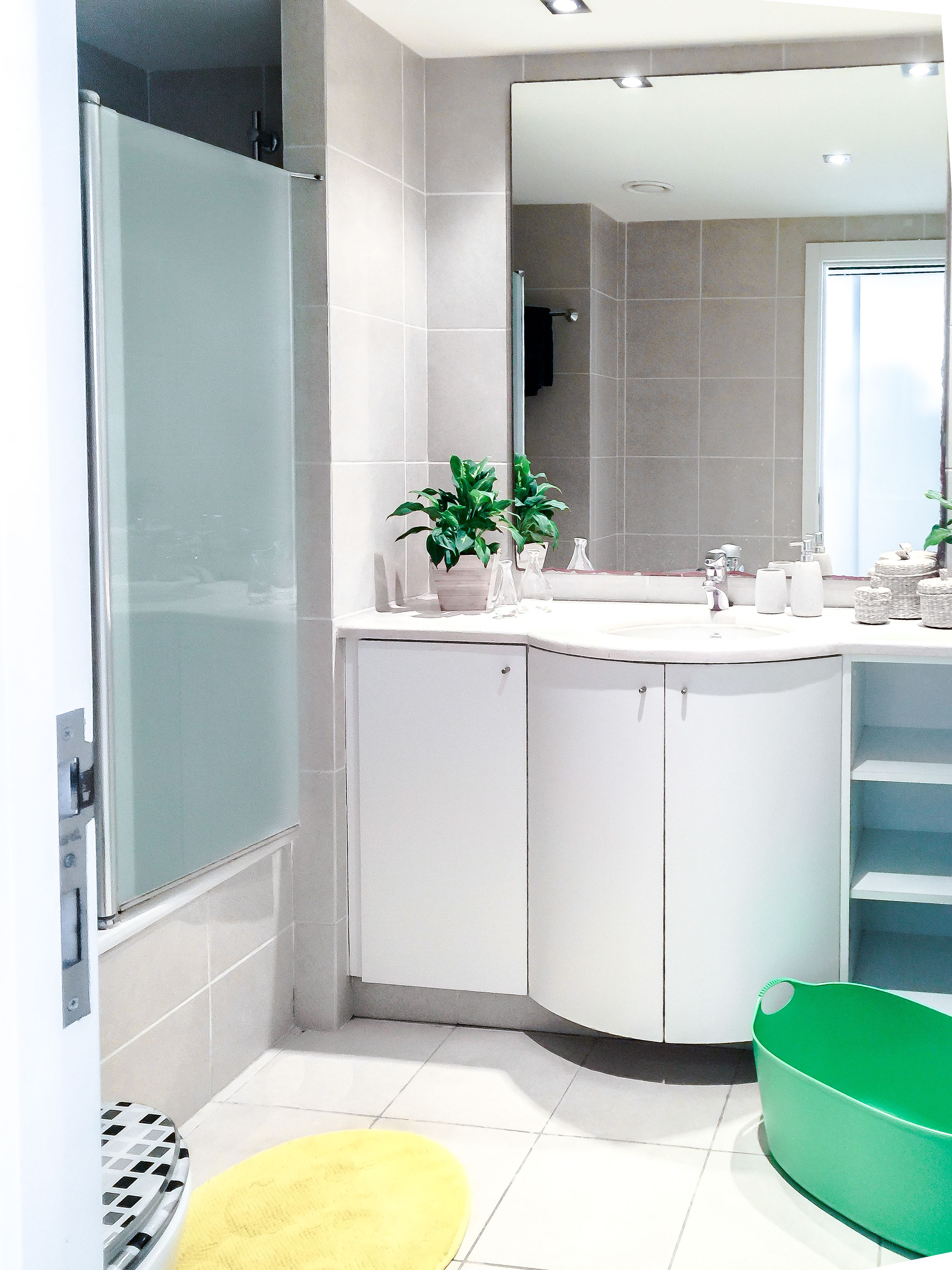 A modern bathroom with a shower, a sink with a mirror, and a green basket.