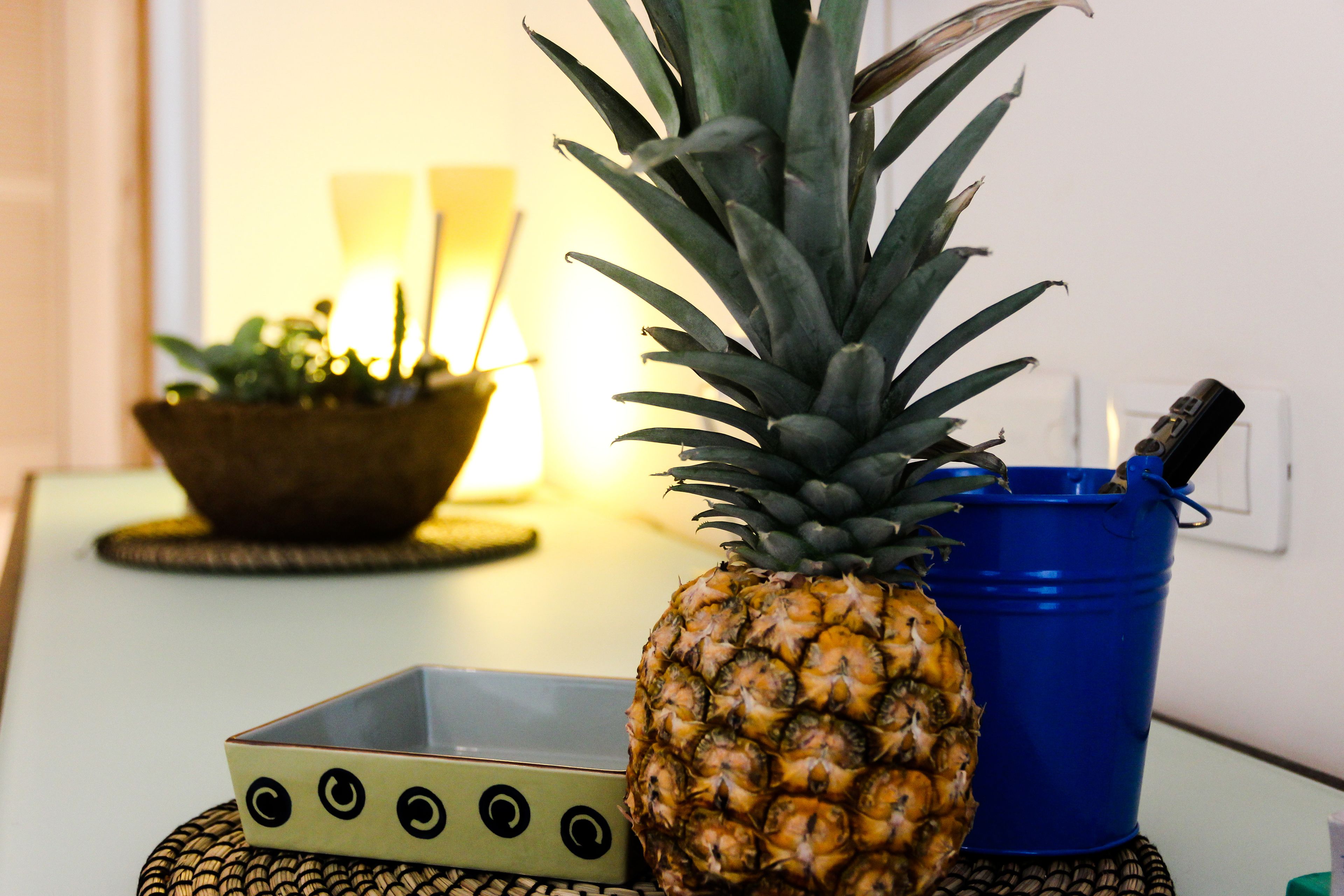 A pineapple on a table with a blue bucket and a decorative bowl.