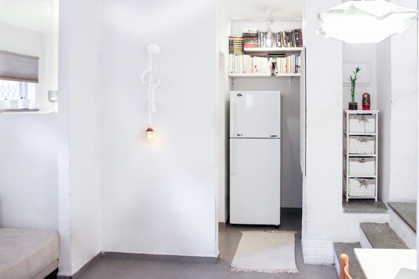 Una cocina compacta con un refrigerador blanco, una pequeña estantería y una lámpara colgante.