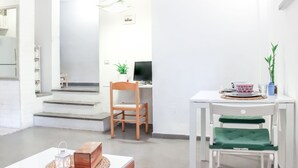 A modern, well-lit room with a wooden chair, a desk with a computer, and a small table with a plant. - Chic Central TLV 1BR Near the Beach (Tel Aviv)